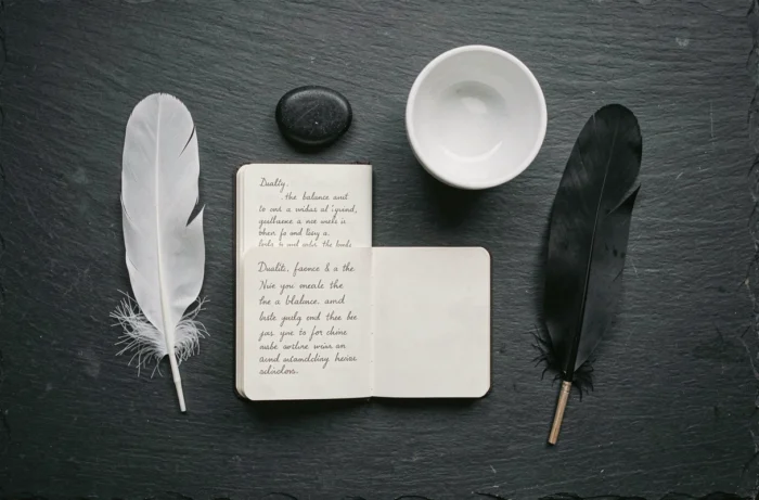 Composition à plat avec plumes blanche et noire, pierre, carnet et bol en céramique, évoquant l'équilibre symbolique des contraires